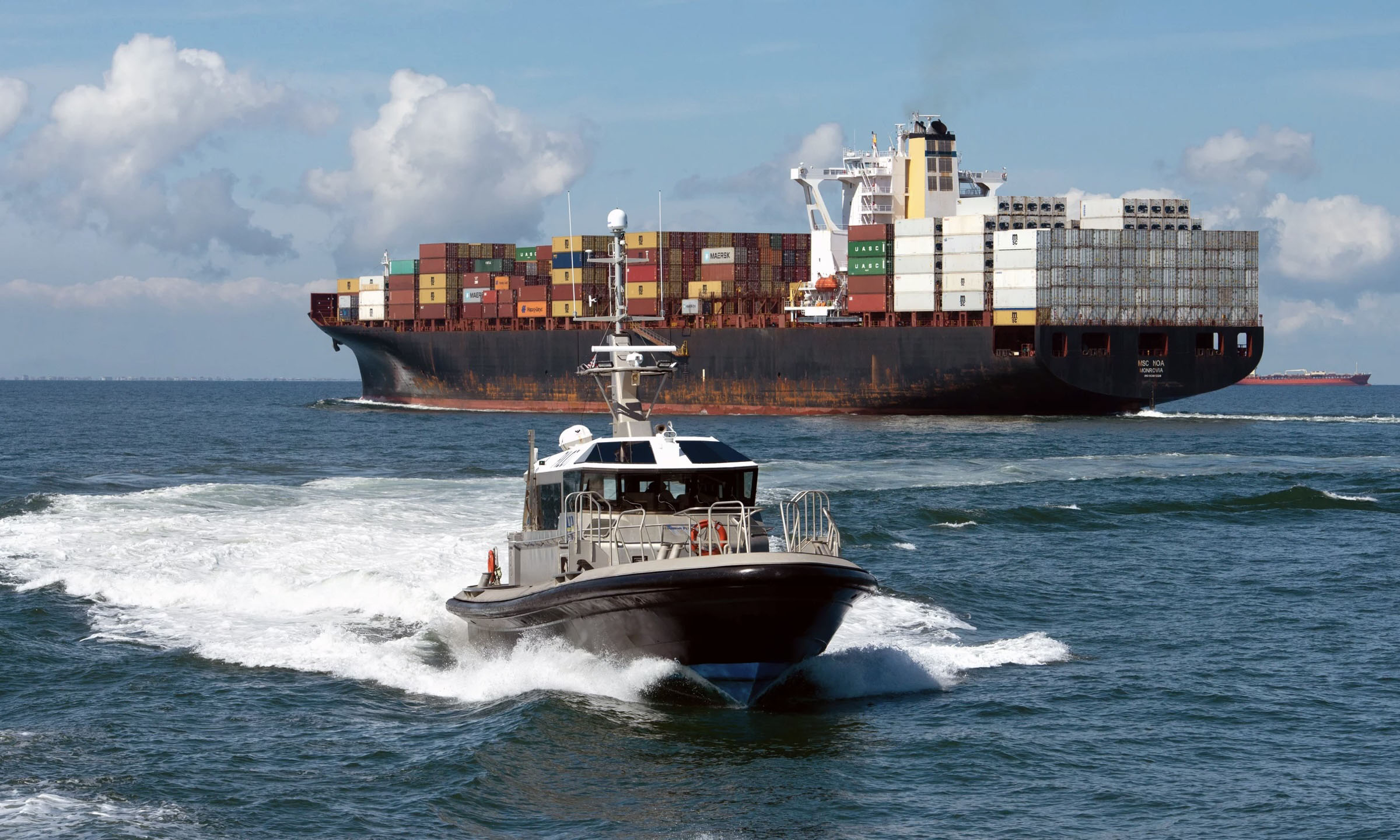 a container ship out at sea with a tug boat in the foreground
